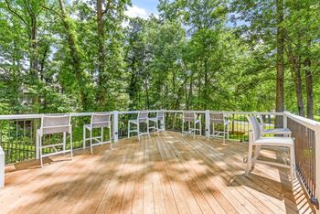 A wooden deck with white chairs and a railing overlooking a forest.